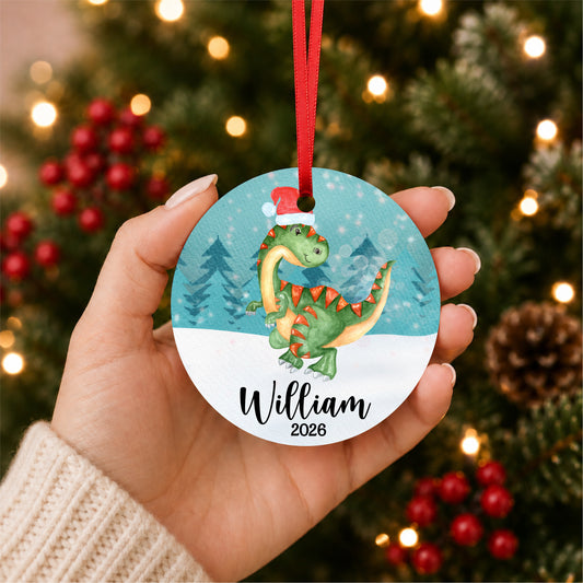 Personalized watercolor Christmas dinosaur ornament with child's name and year, held in hand beside a Christmas tree