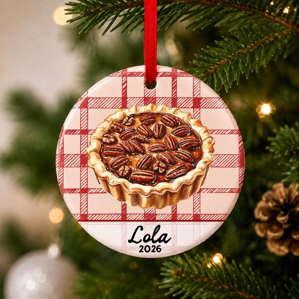Close-up of the personalized pecan pie ceramic ornament with name and year on red plaid hanging on a Christmas tree