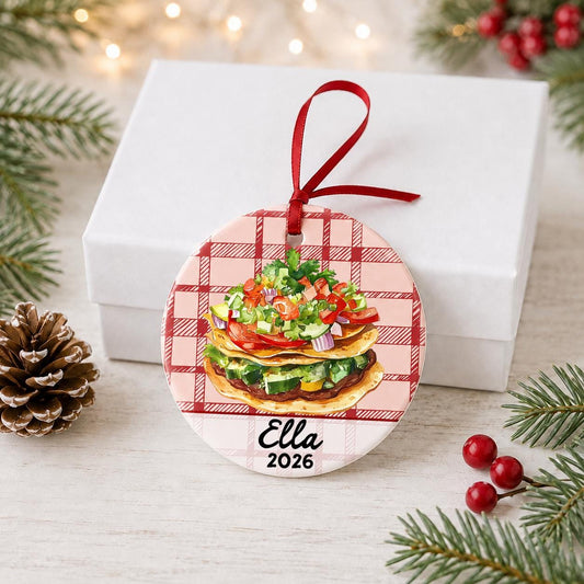 Personalized tostada ceramic ornament with name and year on red plaid in front of a white gift box with pinecones and red berries