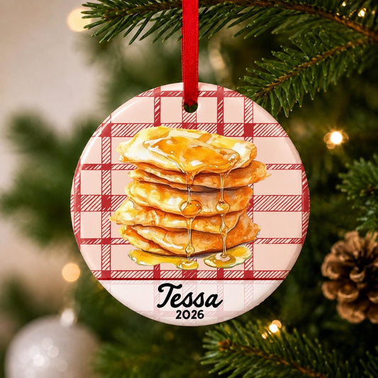 Close-up of the personalized buñuelos ceramic ornament with name and year on red plaid hanging on a Christmas tree