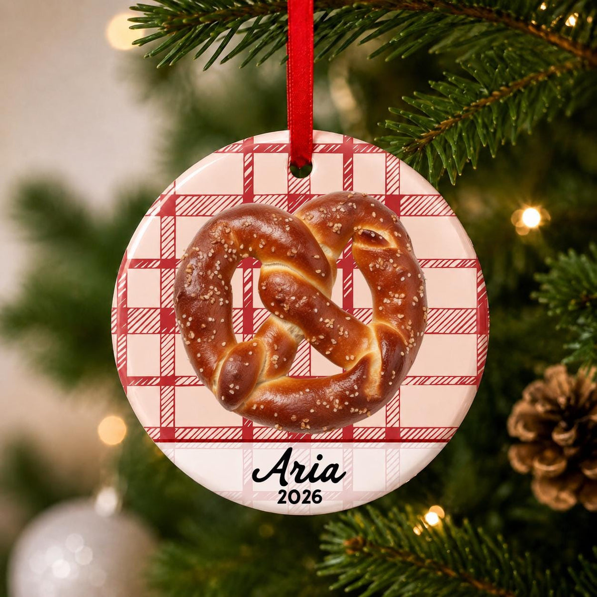 Close-up of the personalized soft pretzel ceramic ornament with name and year on red plaid hanging on a Christmas tree