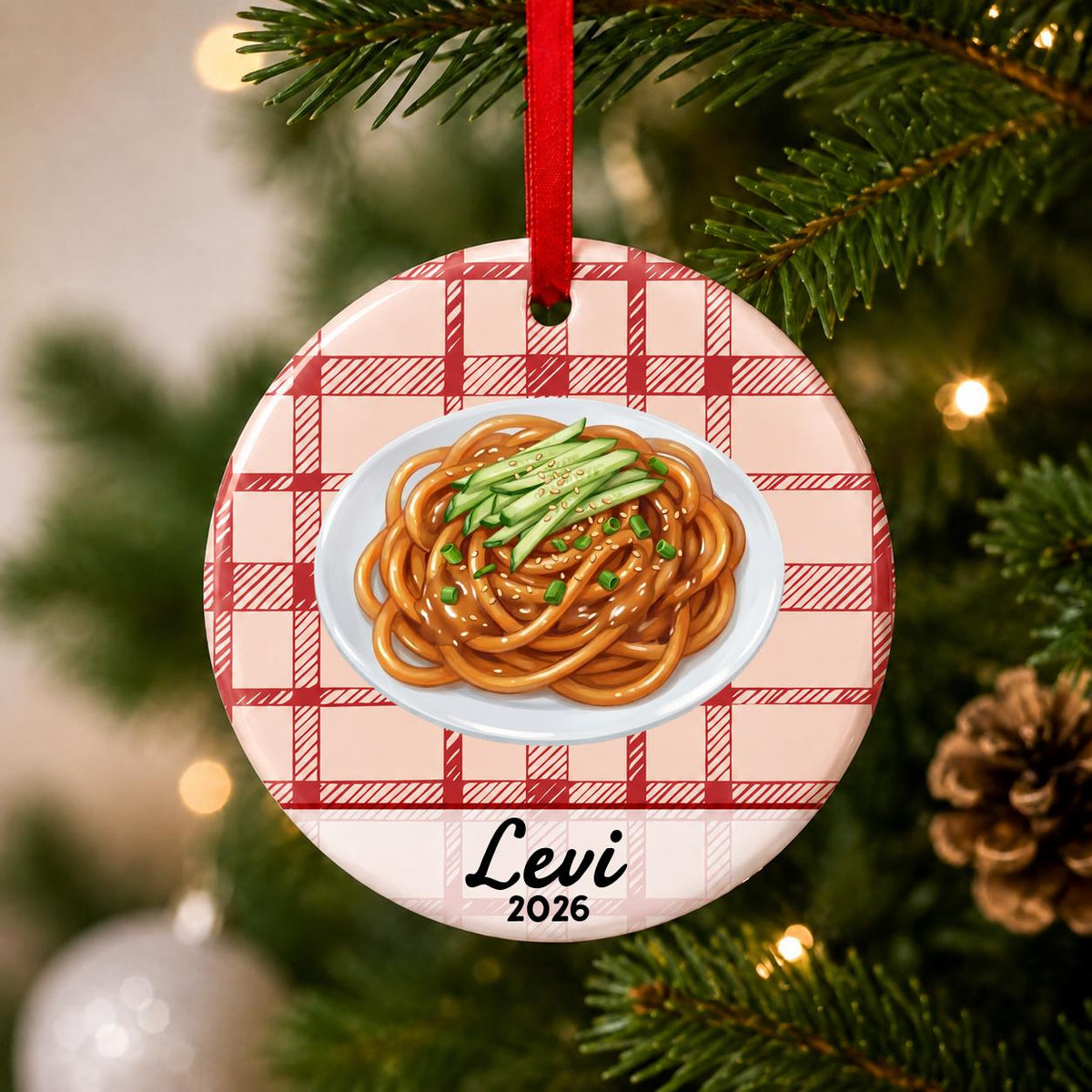 Close-up of the personalized sesame noodles ceramic ornament with name and year on red plaid hanging on a Christmas tree