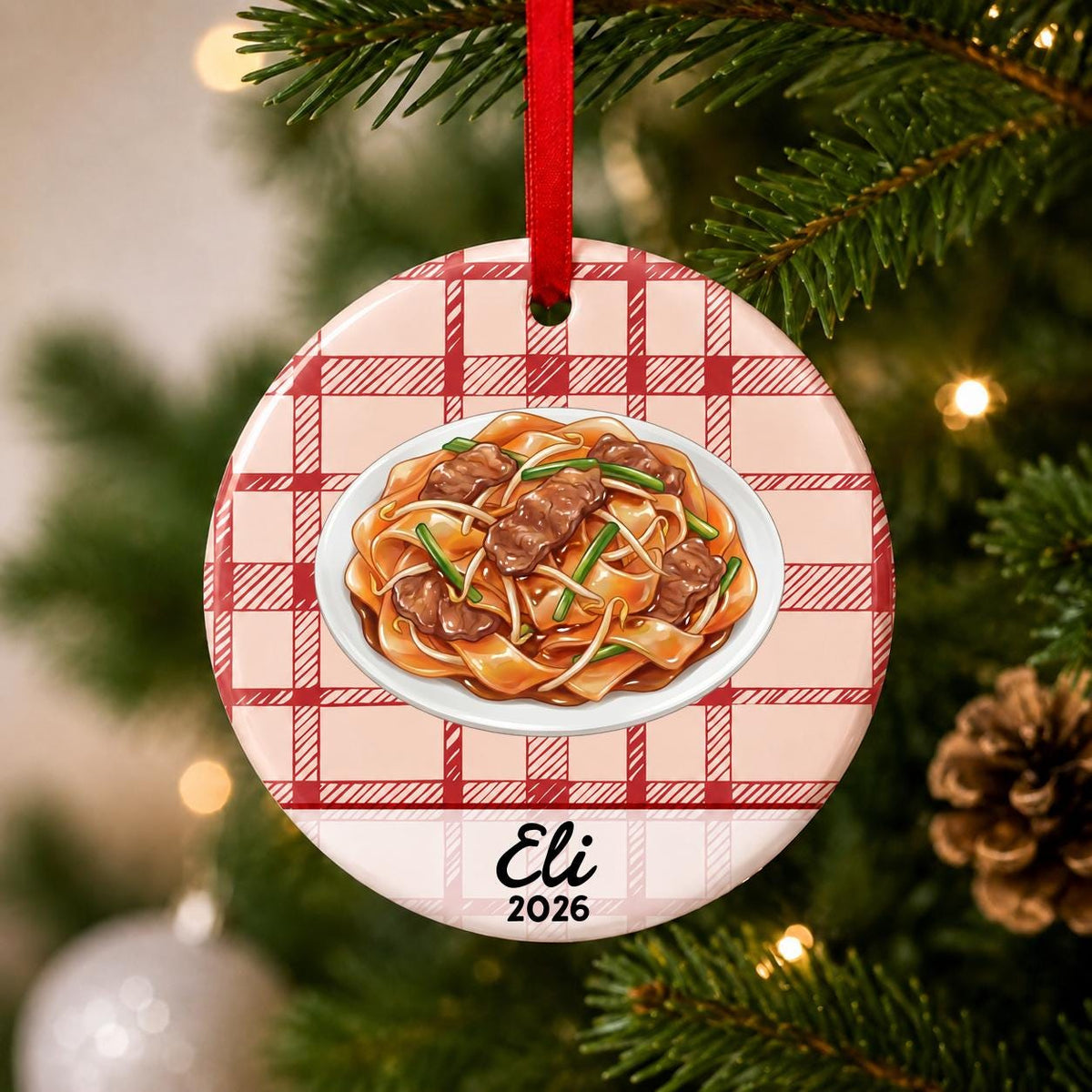 Close-up of the personalized beef chow fun ceramic ornament with name and year on red plaid hanging on a Christmas tree