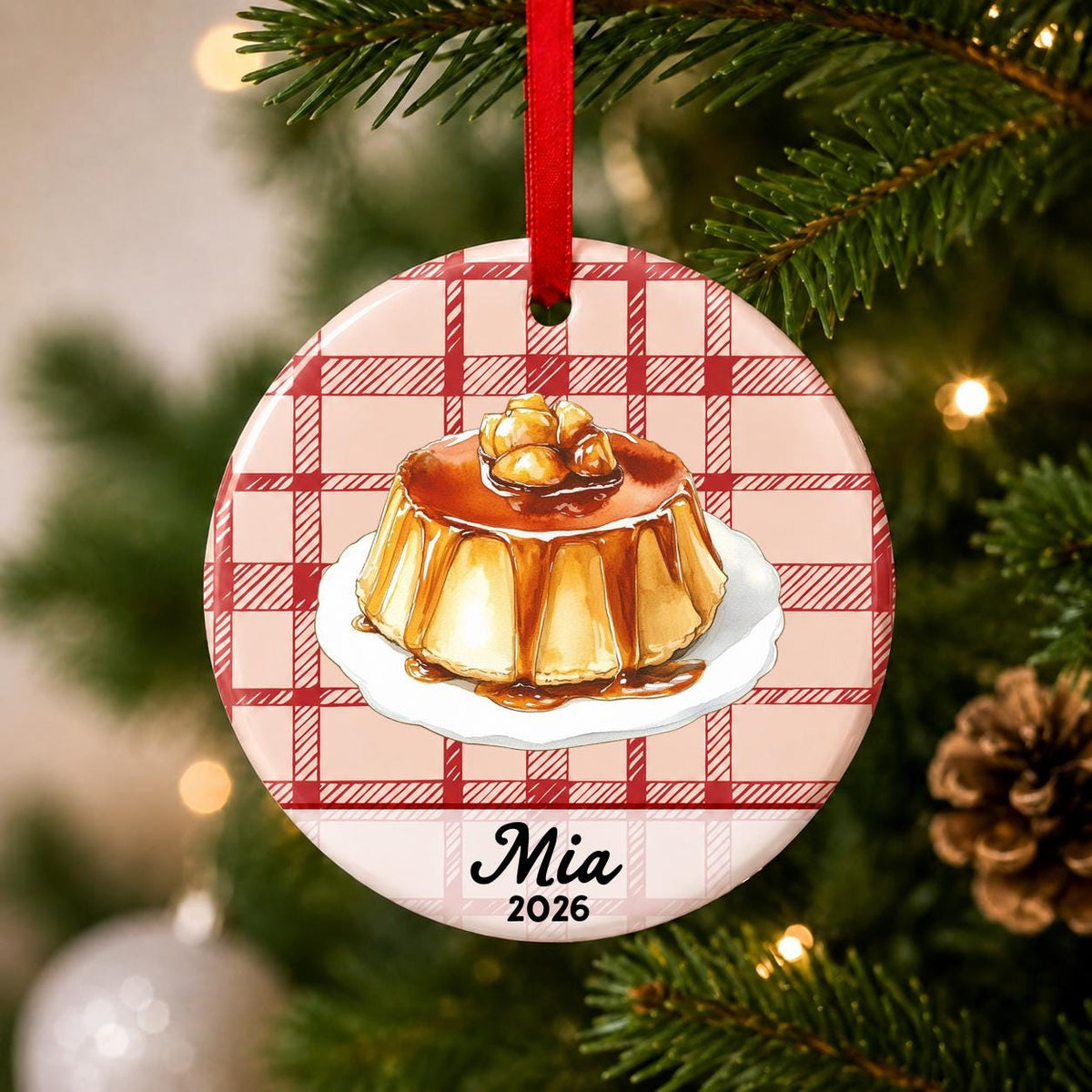 Close-up of the personalized flan ceramic ornament with name and year on red plaid hanging on a Christmas tree