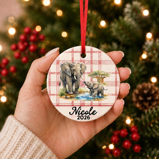 Hand holding the personalized African elephant ceramic ornament with name and year on red plaid in front of a Christmas tree