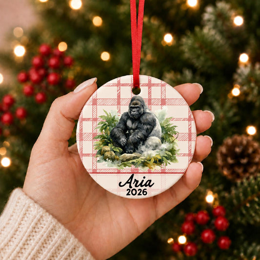 Hand holding the personalized silverback gorilla ceramic ornament with name and year on red plaid in front of a Christmas tree