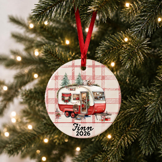 Vintage camper ornament hanging on a decorated Christmas tree with red ribbon and personalized name and year