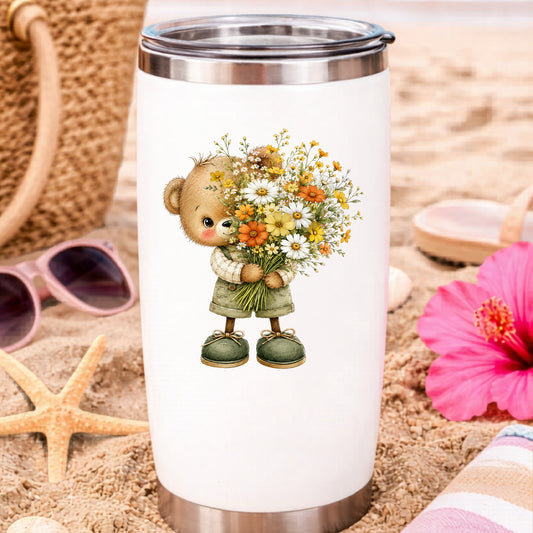 Brown Bear In Overalls Holding Daisy Bouquet UV DTF sticker applied to a white travel tumbler on beach sand