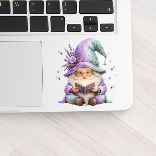 Lavender Reading Gnome With Fireflies UV DTF sticker applied to a silver laptop beside the keyboard