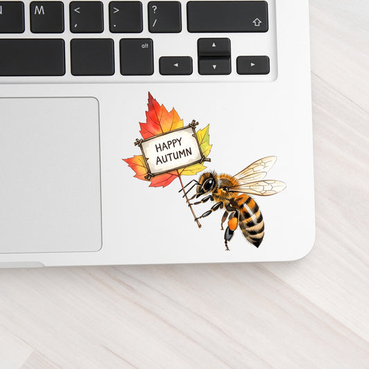 Honeybee Holding Happy Autumn Sign UV DTF sticker applied to a silver laptop beside the keyboard
