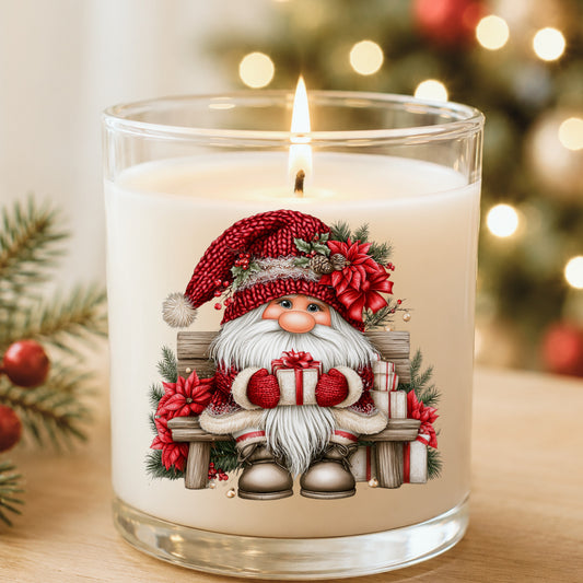 Gnome Sitting On Bench With Poinsettias UV DTF sticker applied to a white candle in a glass holder near Christmas lights