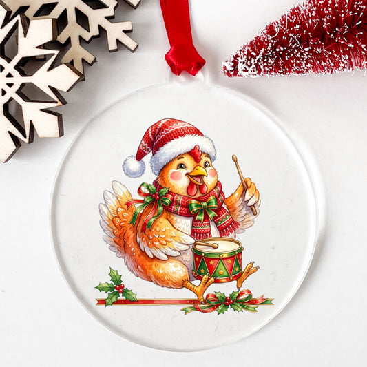 Rooster Playing Christmas Drum UV DTF sticker applied to a clear round acrylic ornament with a red ribbon