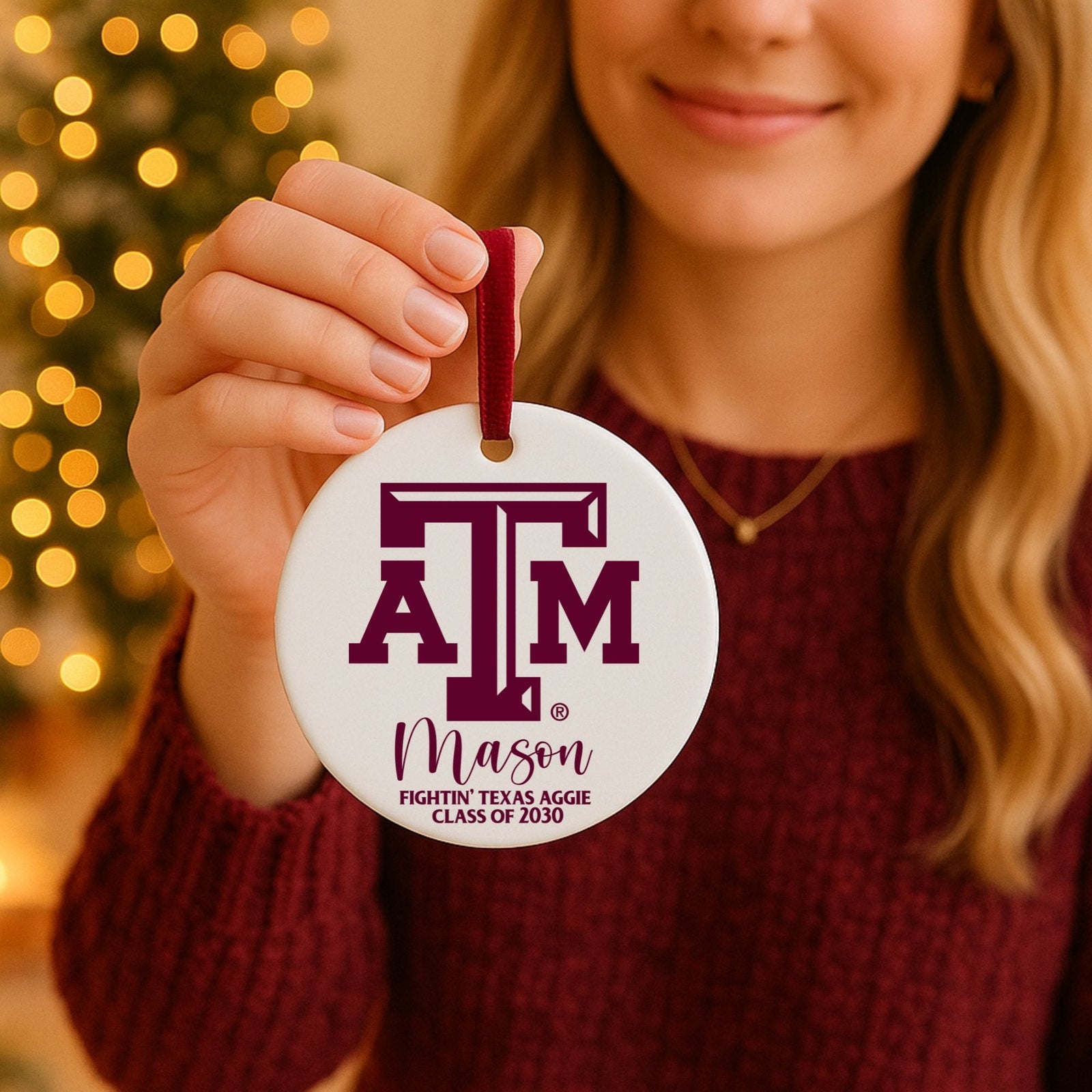 Woman holding Texas A&M personalized ceramic ornament with maroon ribbon in front of a Christmas tree.