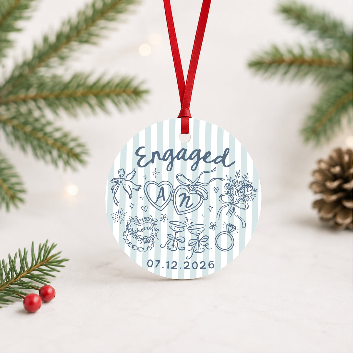 Personalized blue striped engagement ornament with initials and full date, hanging in a bright evergreen setting
