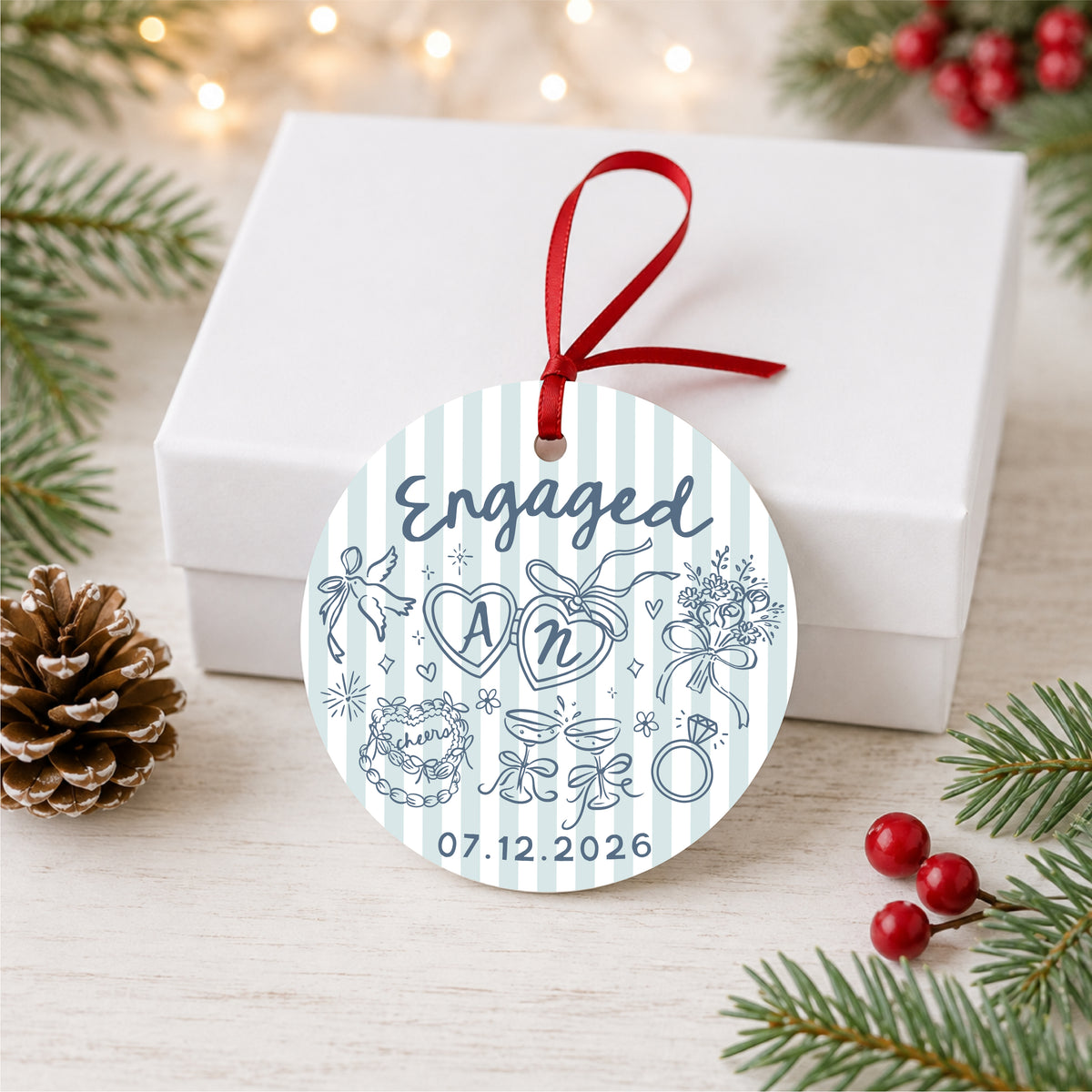 Personalized blue striped engagement ornament with initials and full date, displayed beside a white gift box