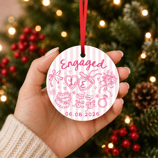 Personalized pink striped engagement ornament with initials and full date, held in hand beside a Christmas tree