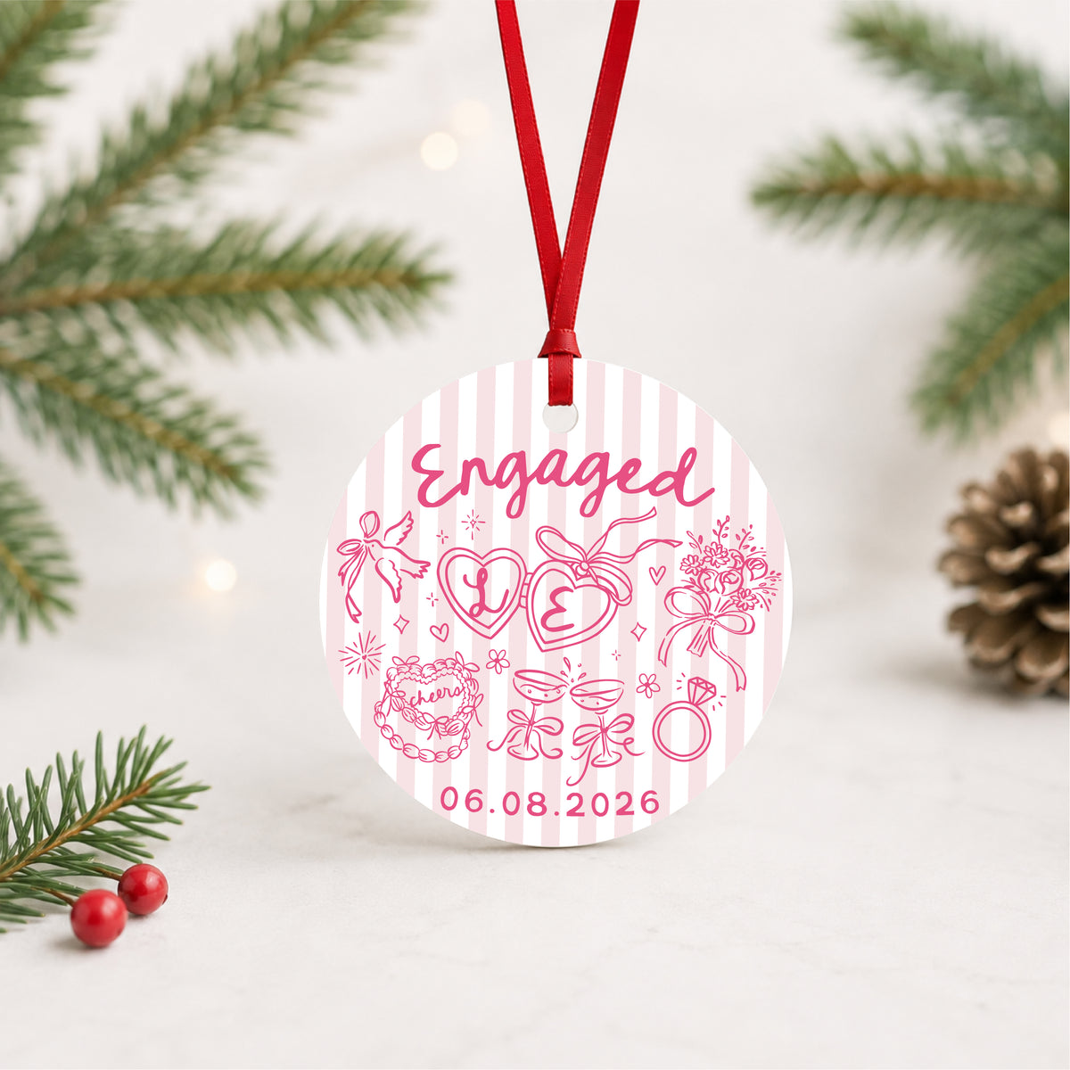 Personalized pink striped engagement ornament with initials and full date, hanging in a bright evergreen setting