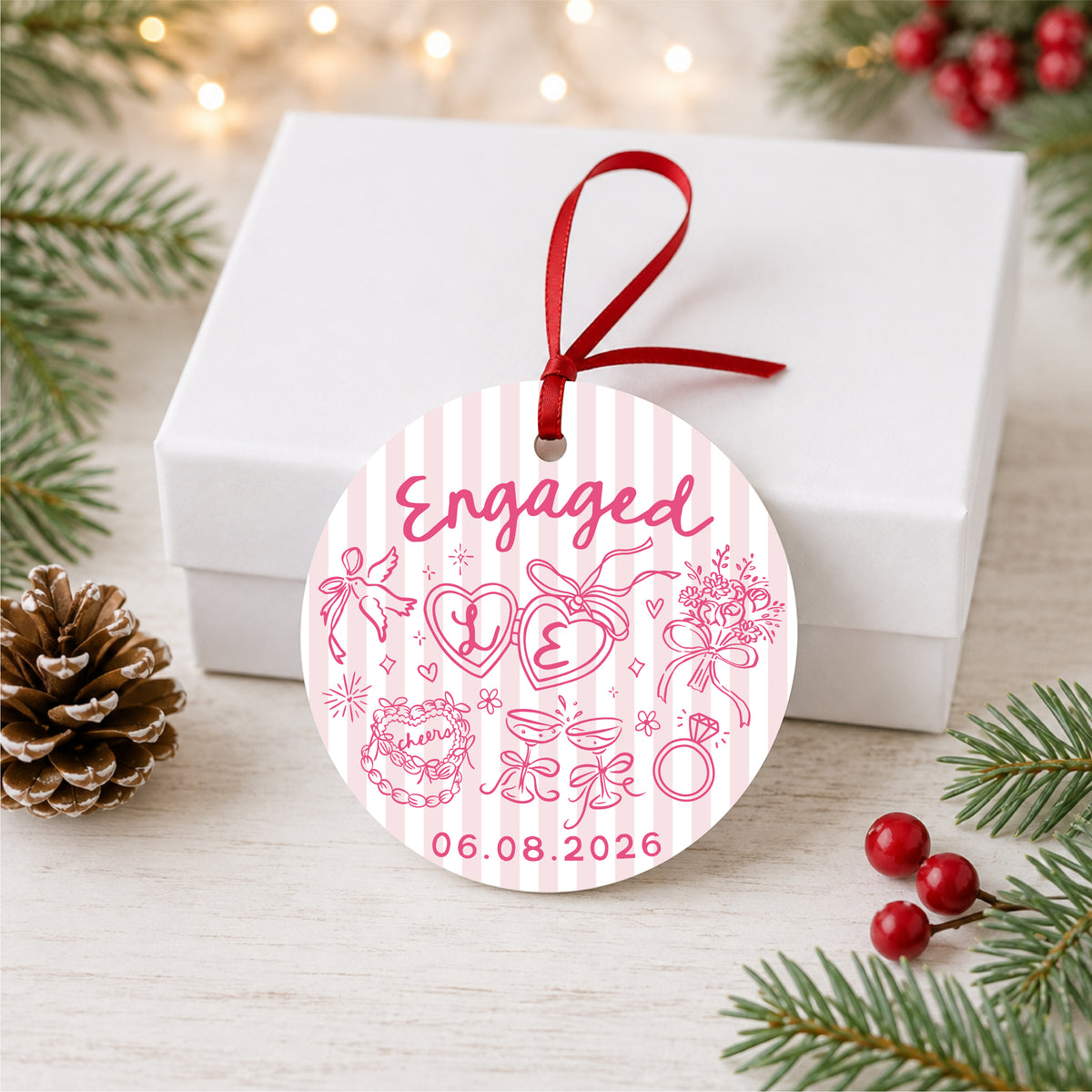 Personalized pink striped engagement ornament with initials and full date, displayed beside a white gift box