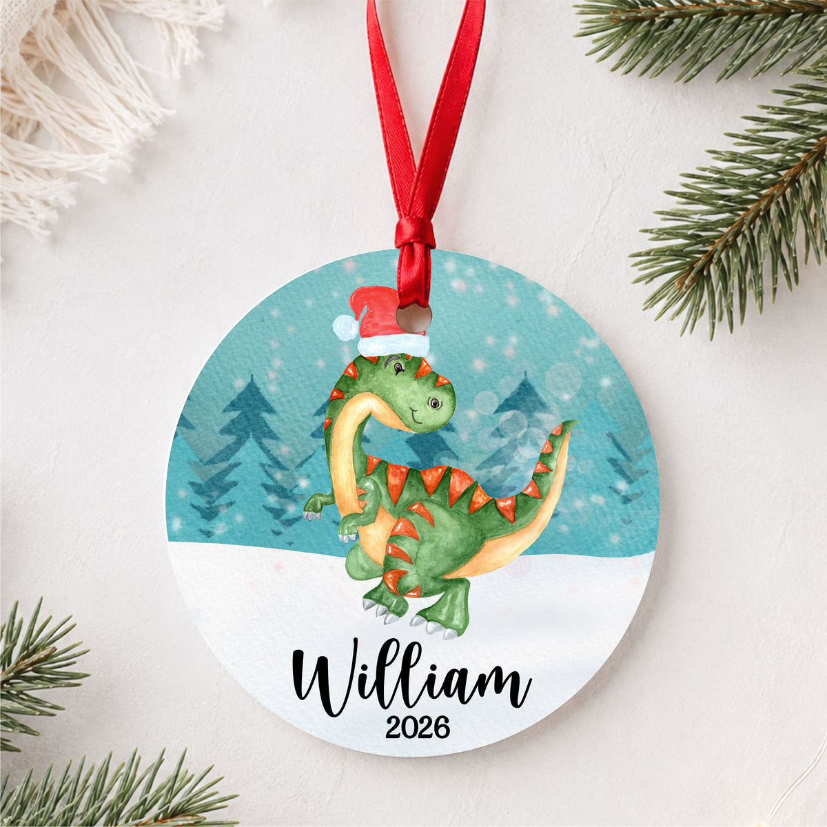 Personalized watercolor Christmas dinosaur ornament with child's name and year, styled flat lay hero view