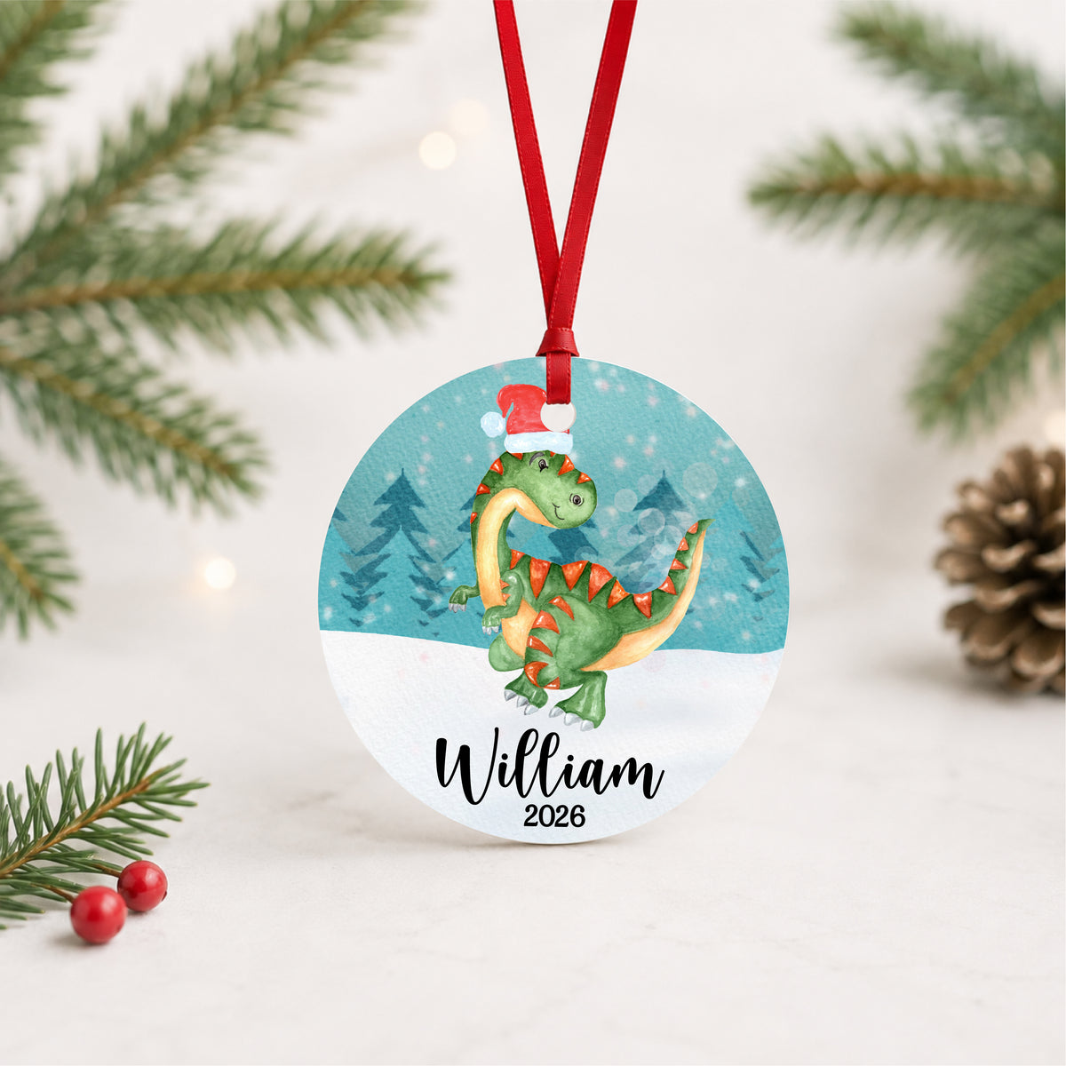Personalized watercolor Christmas dinosaur ornament with child's name and year, hanging in a bright evergreen setting