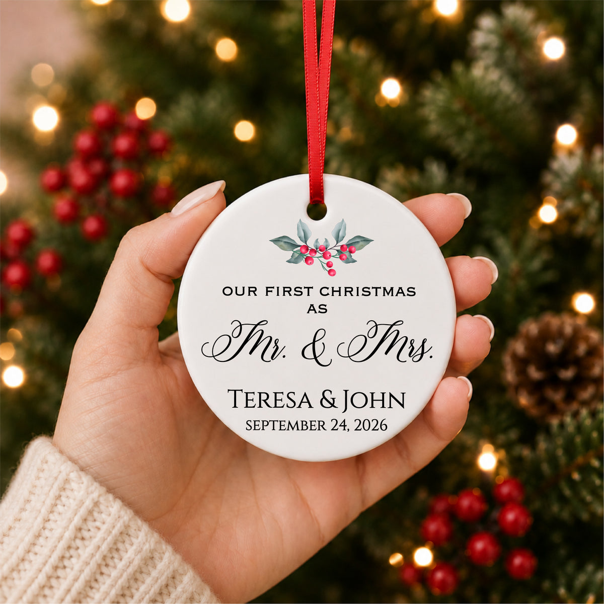 Personalized first Christmas as Mr. and Mrs. ornament with holly, couple names and wedding date, held in hand beside a Christmas tree