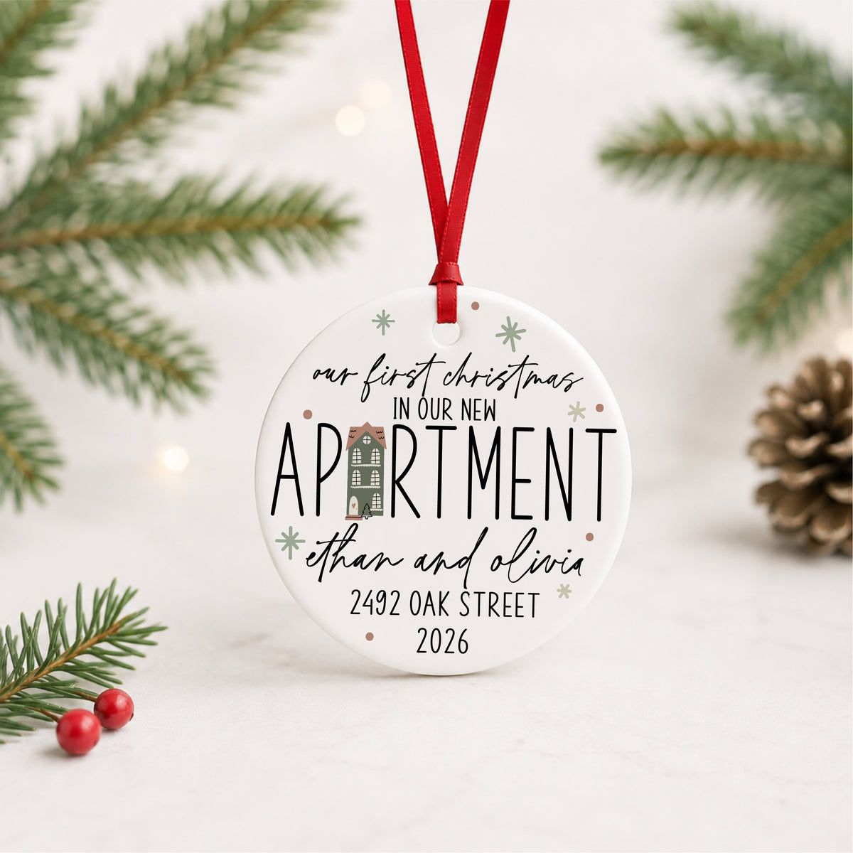 Personalized first Christmas in our new apartment ornament with address, names and year, hanging in a bright evergreen setting