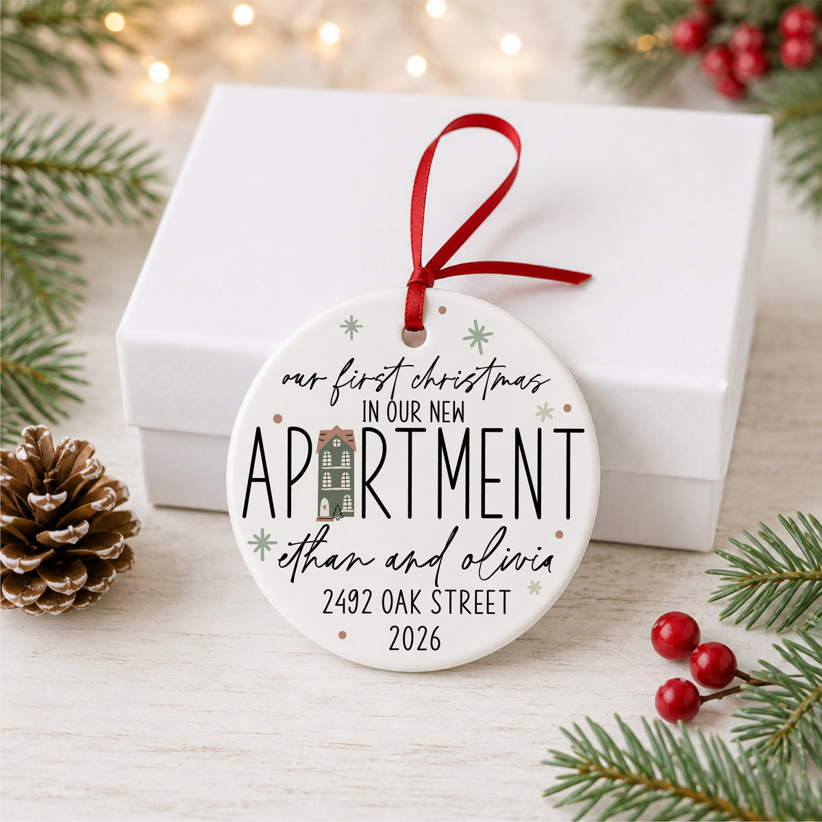 Personalized first Christmas in our new apartment ornament with address, names and year, displayed beside a white gift box