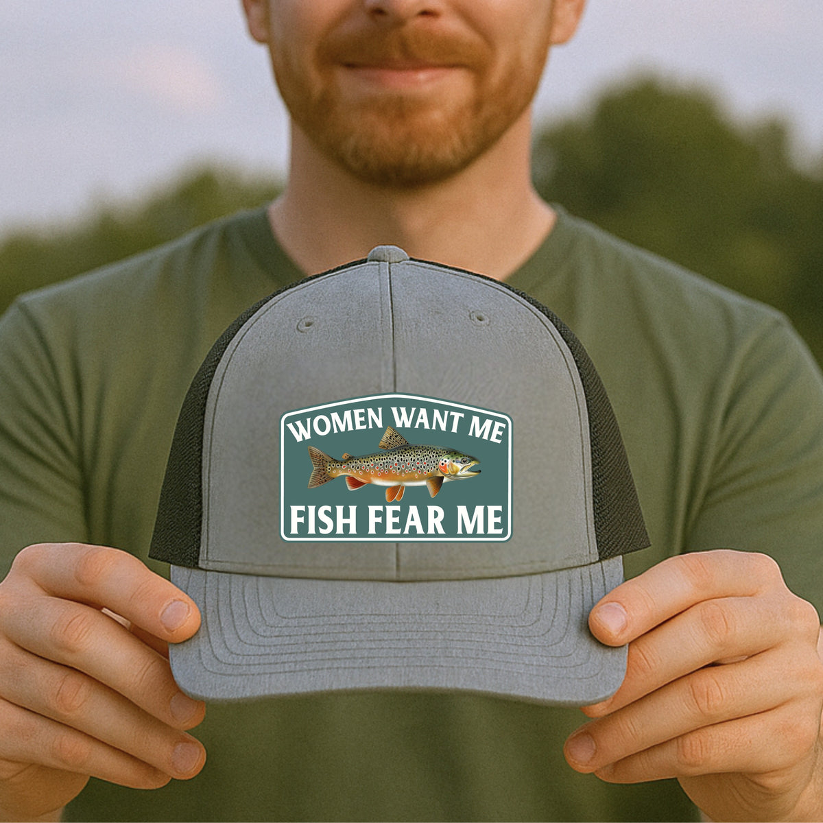 Close-up of hands holding Fish Fear Me Richardson 112 trucker hat showing embroidered patch design