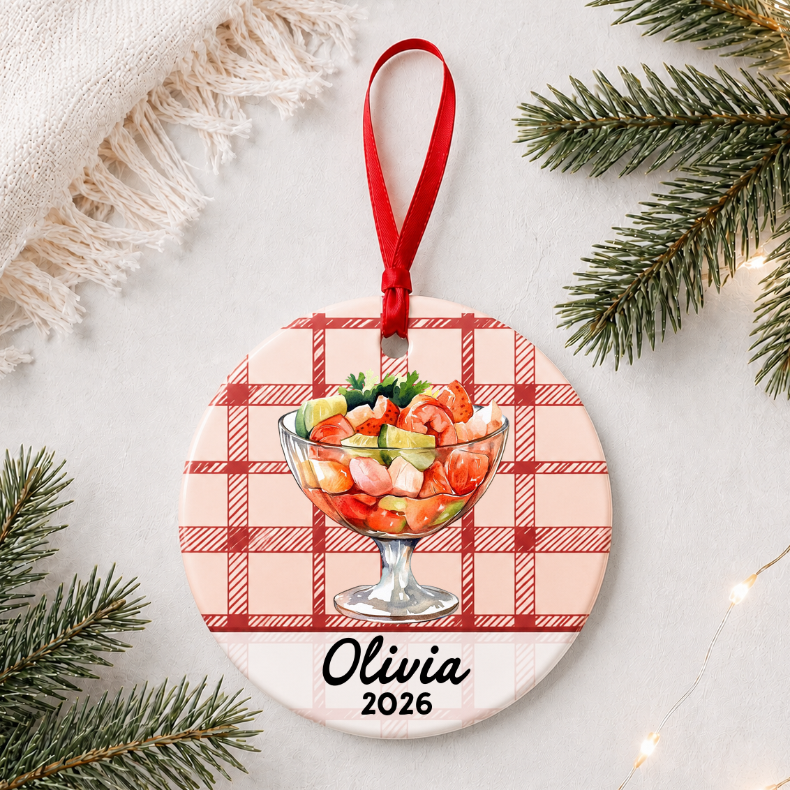 Personalized shrimp cocktail ceramic ornament with name and year on red plaid styled with pine branches on a soft white background