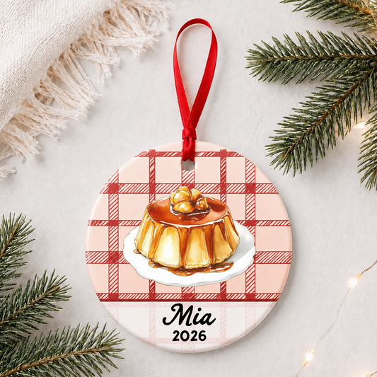 Personalized flan ceramic ornament with name and year on red plaid styled with pine branches on a soft white background