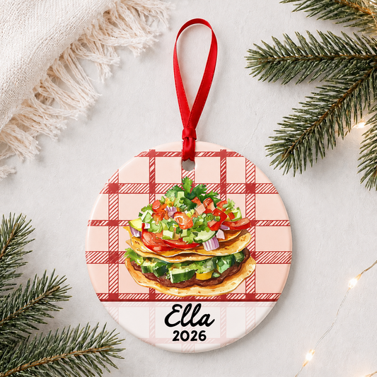 Personalized tostada ceramic ornament with name and year on red plaid styled with pine branches on a soft white background