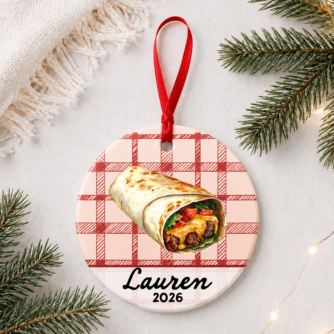 Personalized burrito ceramic ornament with name and year on red plaid styled with pine branches on a soft white background