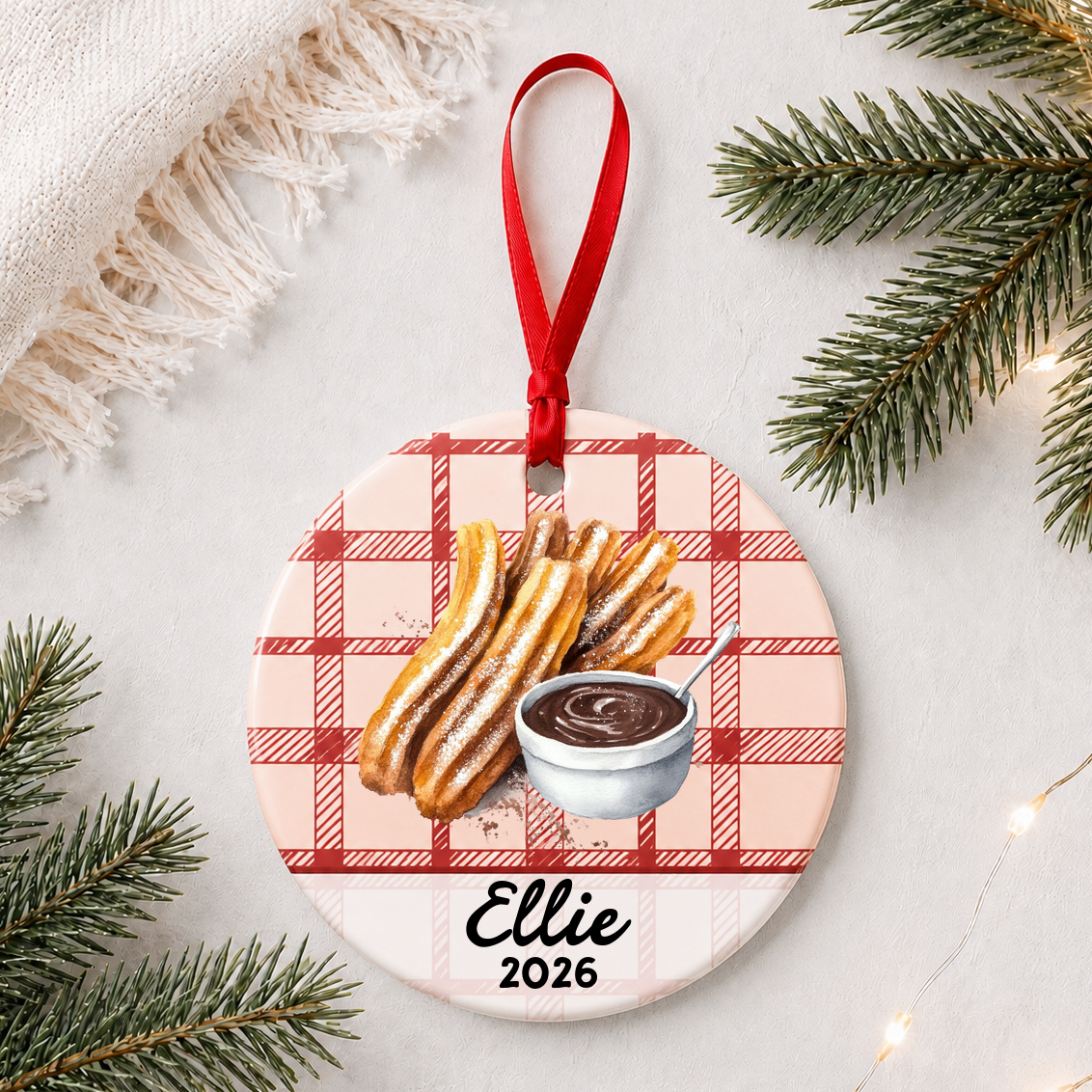 Personalized churro ceramic ornament with name and year on red plaid styled with pine branches on a soft white background