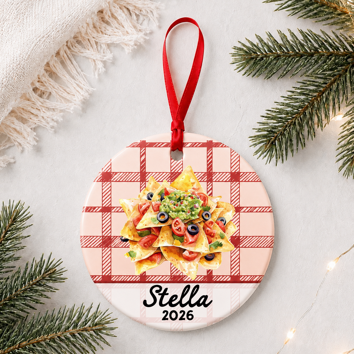 Personalized nachos ceramic ornament with name and year on red plaid styled with pine branches on a soft white background