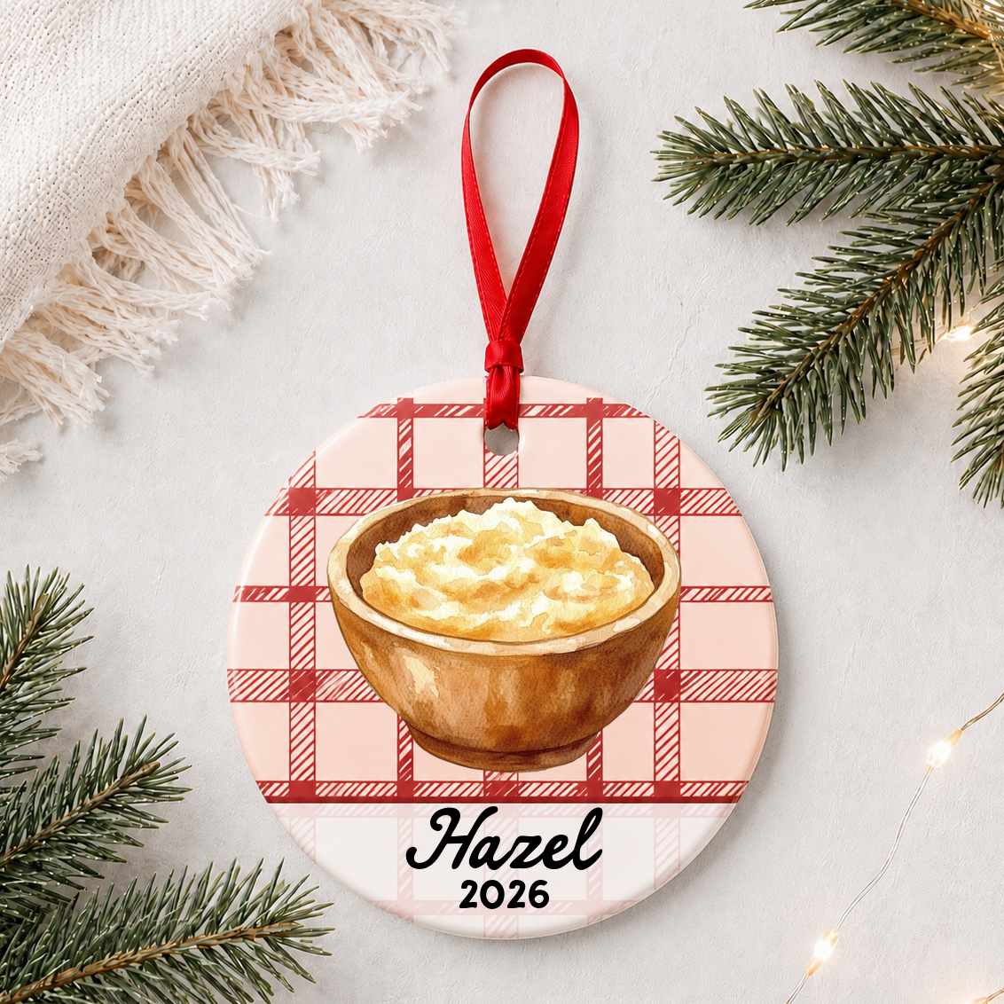Personalized mashed potatoes ceramic ornament with name and year on red plaid styled with pine branches on a soft white background