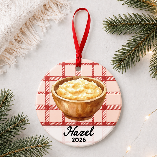 Personalized mashed potatoes ceramic ornament with name and year on red plaid styled with pine branches on a soft white background
