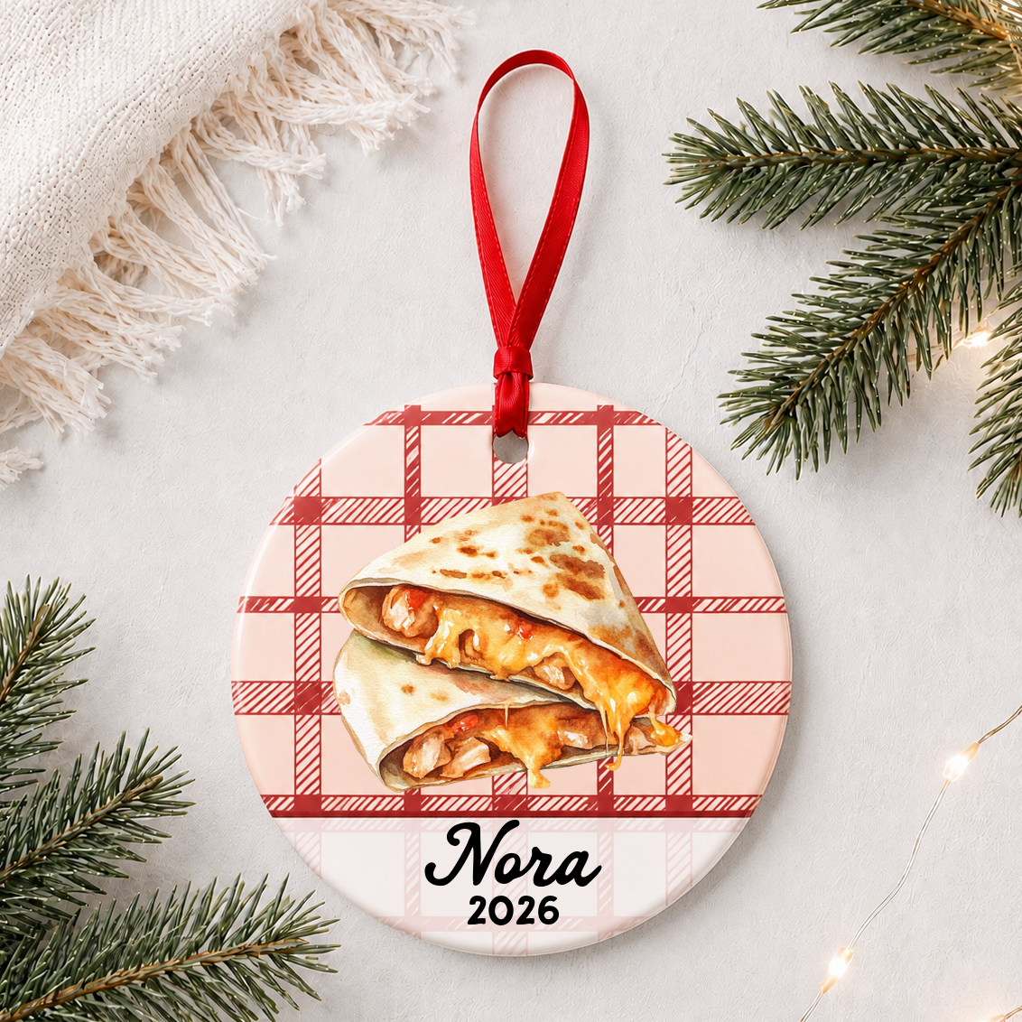 Personalized quesadilla ceramic ornament with name and year on red plaid styled with pine branches on a soft white background
