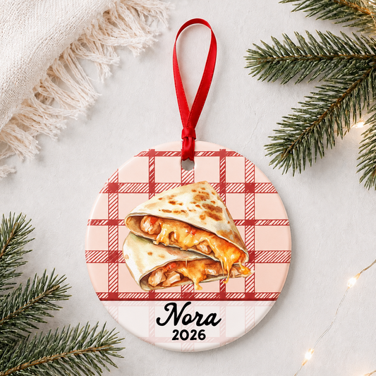 Personalized quesadilla ceramic ornament with name and year on red plaid styled with pine branches on a soft white background