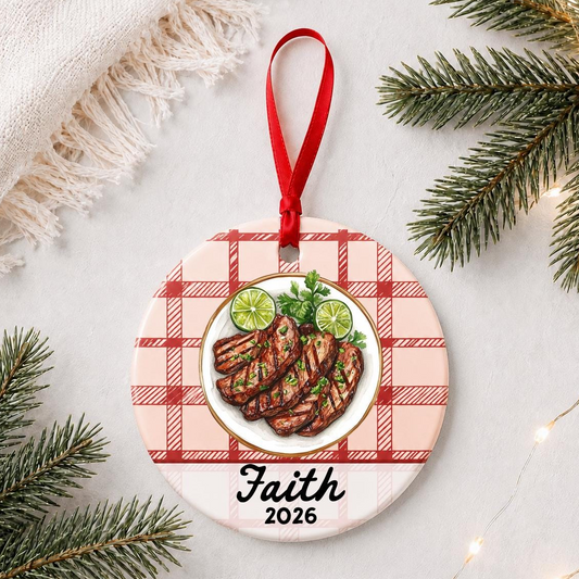 Personalized carne asada ceramic ornament with name and year on red plaid styled with pine branches on a soft white background