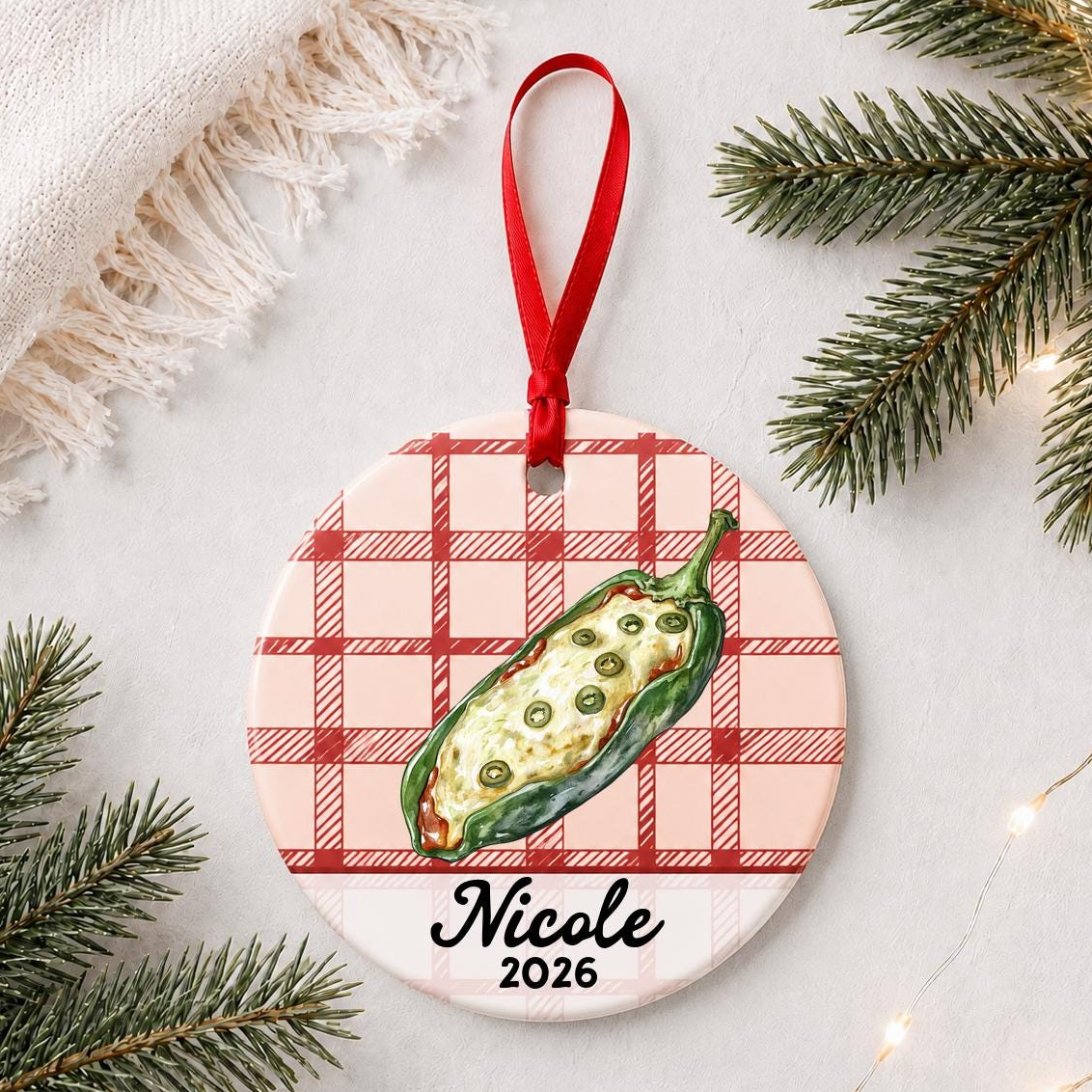Personalized chile relleno ceramic ornament with name and year on red plaid styled with pine branches on a soft white background