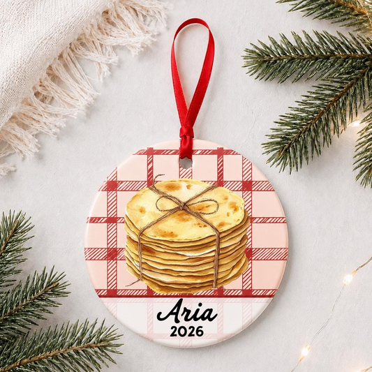 Personalized tortilla ceramic ornament with name and year on red plaid styled with pine branches on a soft white background