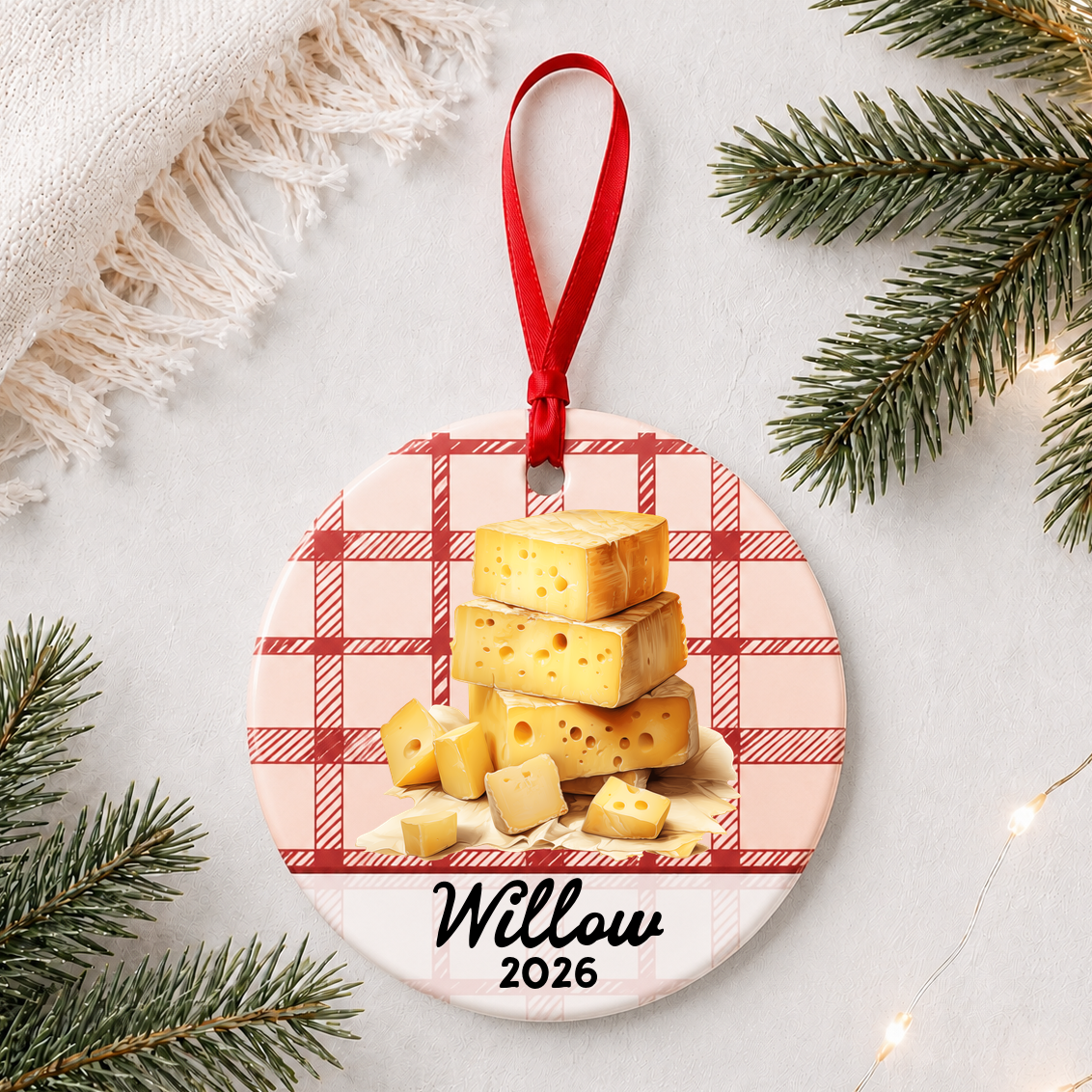 Personalized Swiss cheese ceramic ornament with name and year on red plaid styled with pine branches on a soft white background