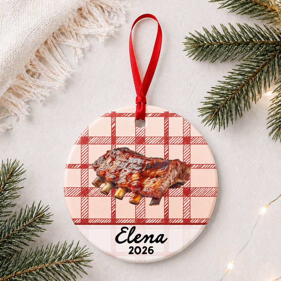 Personalized BBQ ribs ceramic ornament with name and year on red plaid styled with pine branches on a soft white background