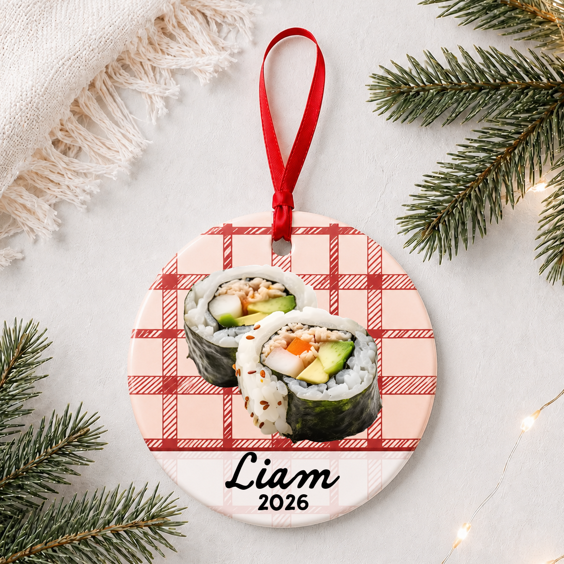 Personalized sushi ceramic ornament with name and year on red plaid styled with pine branches on a soft white background