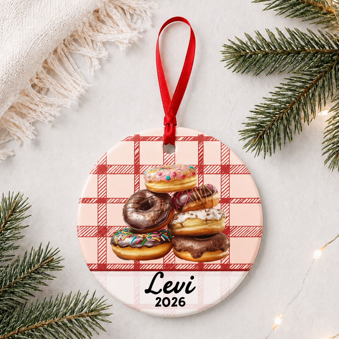 Personalized donuts ceramic ornament with name and year on red plaid styled with pine branches on a soft white background