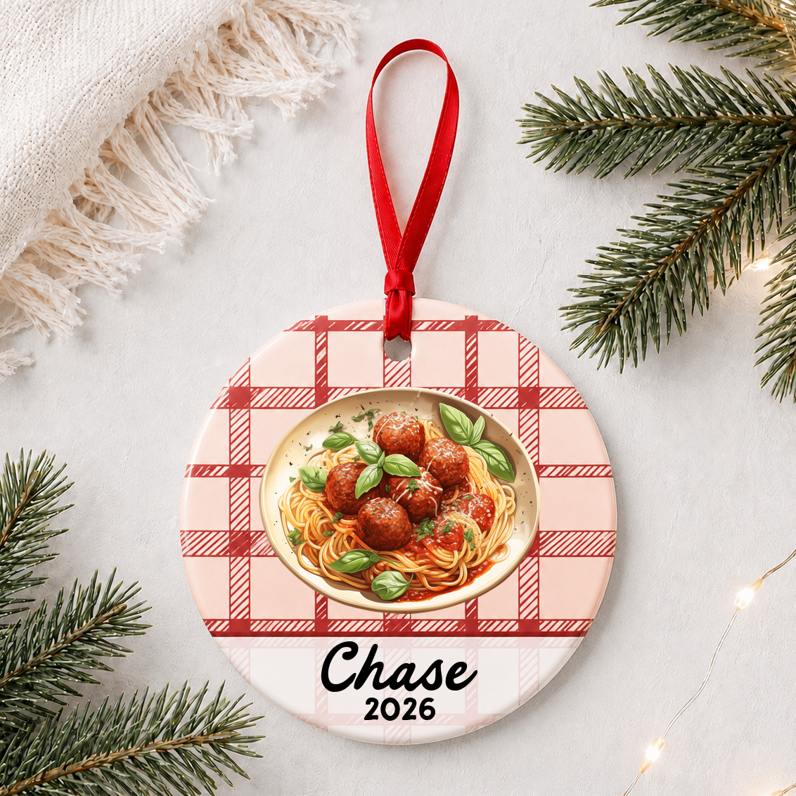 Personalized spaghetti and meatballs ceramic ornament with name and year on red plaid styled with pine branches on a soft white background