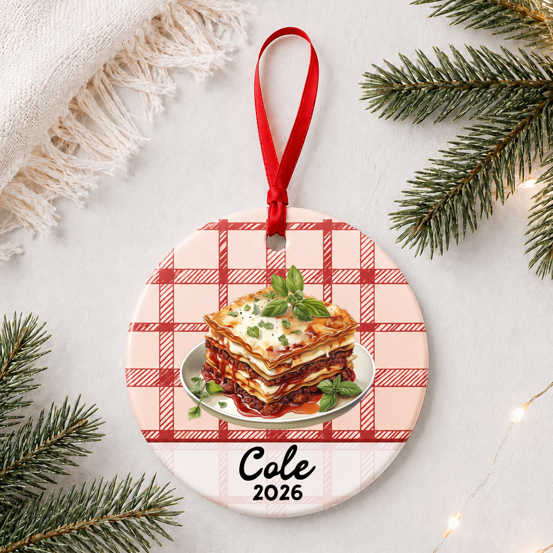 Personalized lasagna ceramic ornament with name and year on red plaid styled with pine branches on a soft white background
