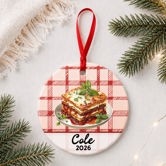 Personalized lasagna ceramic ornament with name and year on red plaid styled with pine branches on a soft white background