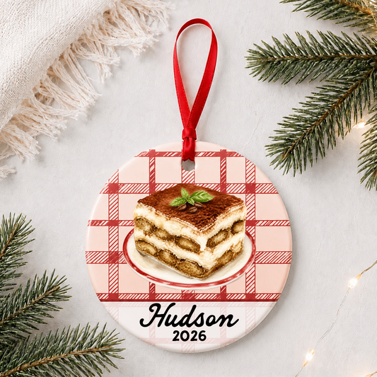 Personalized tiramisu ceramic ornament with name and year on red plaid styled with pine branches on a soft white background