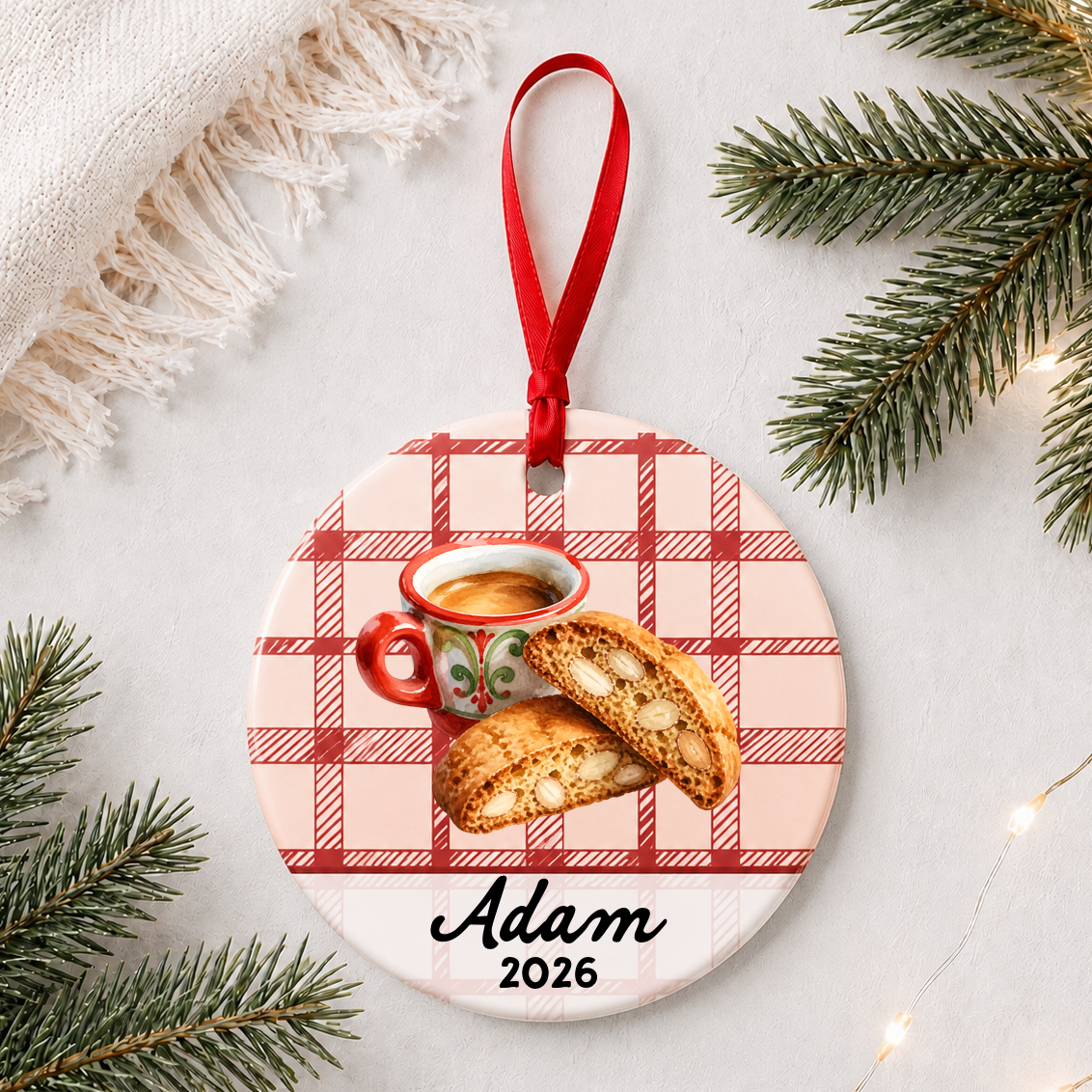 Personalized espresso and biscotti ceramic ornament with name and year on red plaid styled with pine branches on a soft white background